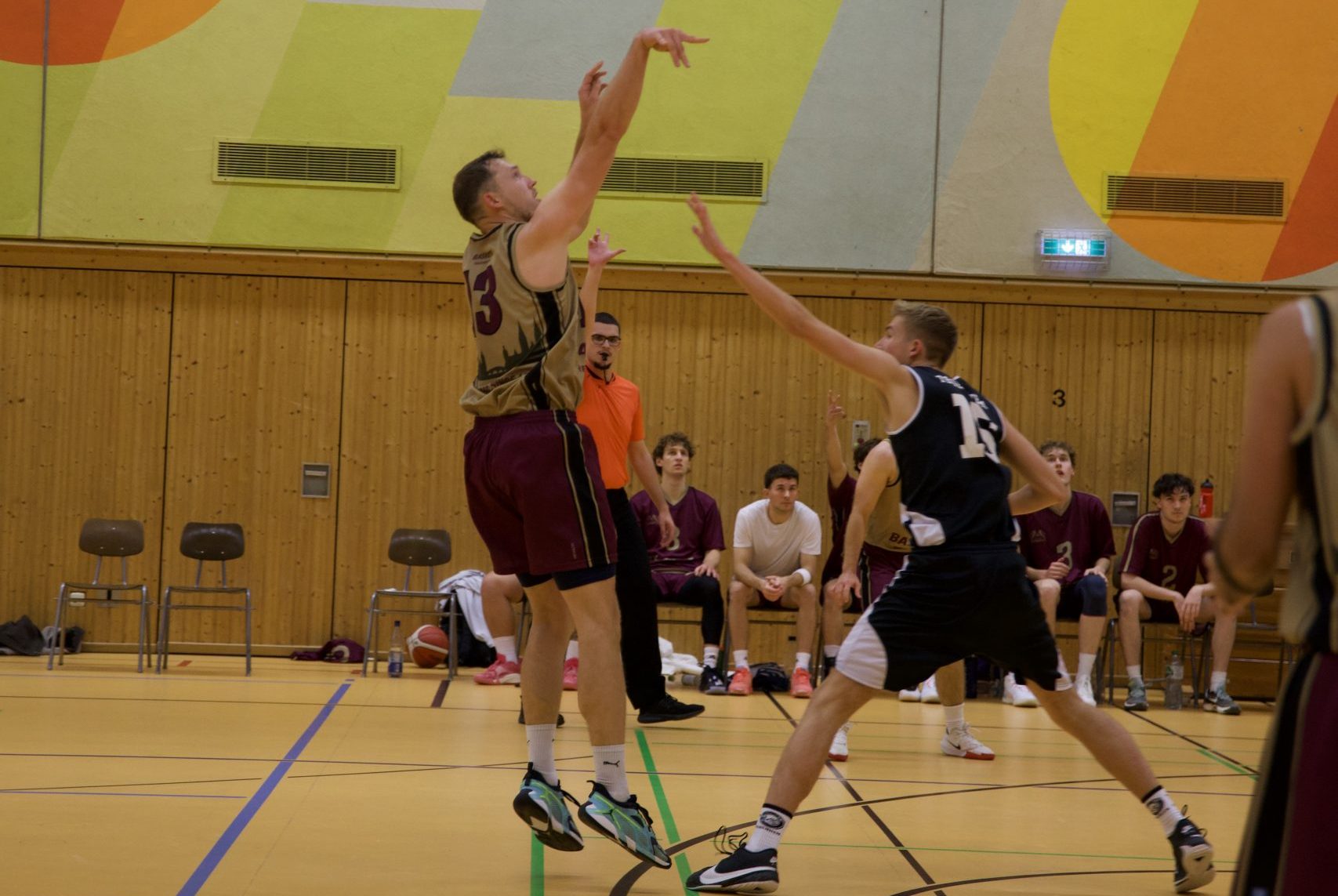 Basketball Spieler wirft einen 3 Punkte Wurf mit der Spielerbank im Hintergrund