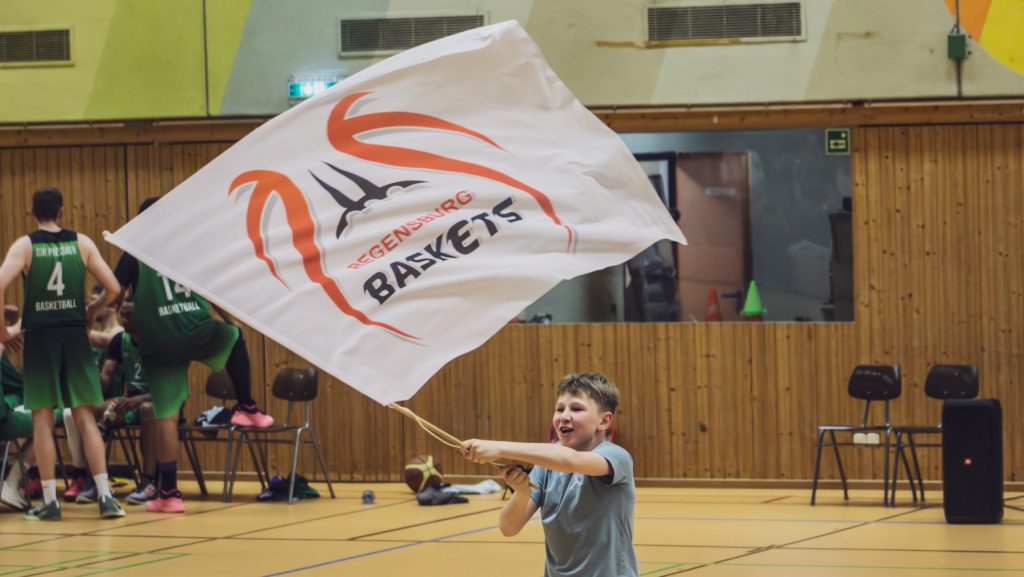 Kind schwingt eine Flagge der Regensburg Baskets während eines Basketballspiels